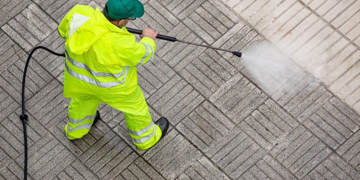 Worker cleaning a pavement sidewalk with high pressure water jet What Is Soft Wash Pressure Washing